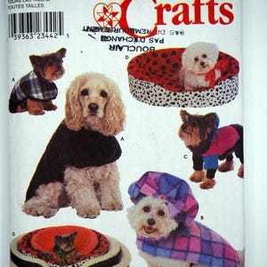 Puede incluir: Patrón de Simplicity Crafts con perros con varios atuendos y camas para perros. Los perros llevan abrigos, suéteres y sombreros a cuadros y de colores lisos. El patrón incluye el texto "Simplicity Crafts" y "Size A All Sizes".