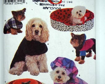 May include: Simplicity Crafts pattern featuring dogs in various outfits and dog beds. The dogs are wearing coats, sweaters, and hats in plaid and solid colors. The pattern includes the text "Simplicity Crafts" and "Size A All Sizes".