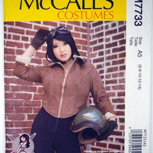 Może przedstawiać: Wzór szycia McCall's Costumes M7733. Wzór przedstawia kobietę w brązowej kurtce lotniczej, czarnych spodniach i kasku. Wzór zawiera oddzielne elementy wzoru na miseczki dla pań A/B, C, D. Rozmiar A5 (6-8-10-12-14).