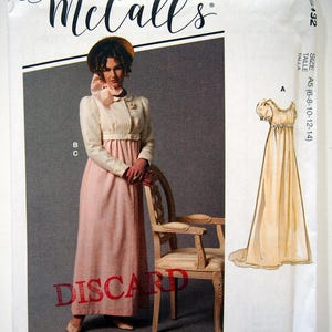 May include: McCall's sewing pattern for a dress, size A5 (6-8-10-12-14). The pattern features a white dress with a pink sash and a white jacket. The model is wearing a straw hat and a white collar.