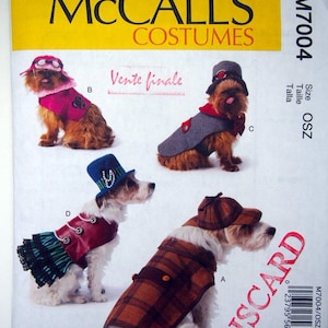 May include: McCall's Costumes pattern showing dog outfits. The image displays four dogs in different costumes: a pink coat with a hat, a grey coat with a hat, a red and green outfit with a blue hat, and a plaid coat with a cap. The word "DISCARD" is printed on the image.