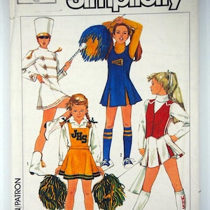 May include: Vintage Simplicity sewing pattern with illustrations of cheerleading and marching band uniforms. The pattern includes designs for a white marching band uniform, and cheerleading outfits in blue, gold, and red.