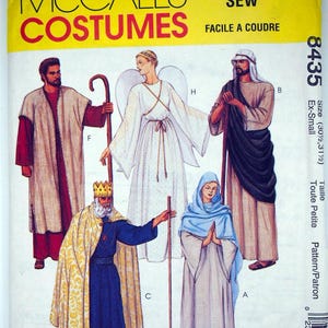 Peut inclure: Patron de costumes McCall's avec des illustrations de personnages bibliques. L'image présente des personnages en robes, dont un ange et un roi. Le patron est étiqueté "Facile à coudre" et comprend des informations de taille.