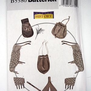 May include: A Butterick B5580 Making History sewing pattern envelope featuring illustrations of various accessories including pouches, gauntlets with scale-like textures, a feathered quill, and a split-leg garment piece, all arranged in a circular layout.
