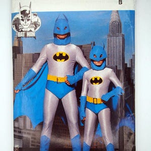 May include: A vintage Butterick sewing pattern for Batman costumes. The cover features two figures in gray and blue Batman suits with the Batman logo. The costumes include masks, capes, and yellow belts. The background shows a cityscape.