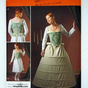May include: A Simplicity sewing pattern envelope 2621 for sizes 16-24. The cover displays a green damask corset, a white long-sleeved shirt, and a full-length beige skirt with horizontal tucks. The pattern includes views A, B, C, and D.