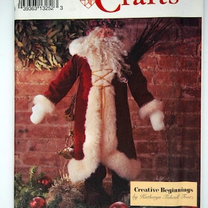 May include: A Simplicity Crafts pattern for a Santa Claus figure. The pattern shows a Santa Claus doll with a red and brown coat, white faux fur trim, and a long white beard. The pattern is labelled "Creative Beginnings by Katheryn Tidwell Foutz."