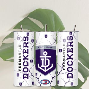 Puede incluir: Tres vasos de acero inoxidable blancos con un diseño morado y blanco que presenta el logotipo de los Fremantle Dockers, el nombre del equipo y el texto "EST. 1994" y "AFL".