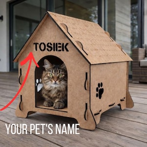 Puede incluir: Una casa de madera marrón para mascotas con el nombre "TOSIEK" recortado en la parte superior. Un gato con ojos verdes está sentado dentro de la casa. Una huella de pata está en el costado. El texto "YOUR PET'S NAME" está en la parte inferior.