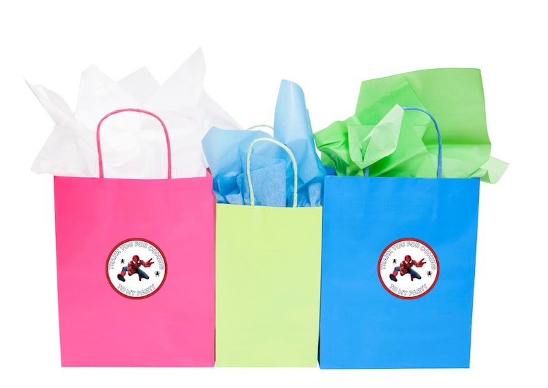 Puede incluir: Tres bolsas de regalo con papel de seda en su interior. Las bolsas son rosa, verde y azul. Cada bolsa tiene una pegatina redonda con un personaje de superh&eacute;roe de dibujos animados y el texto "Gracias por venir a mi fiesta".