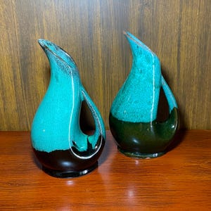 May include: Two ceramic vases with a teal and black glaze. The vases are shaped like a bird with a long neck and a curved spout.