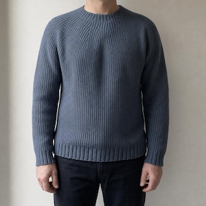 Peut inclure: Un pull à manches longues bleu ardoise doté d'une texture en tricot côtelé épais, d'une encolure ronde et de manches raglan. Le vêtement présente un ourlet et des poignets côtelés ajustés, offrant une silhouette structurée et uniforme.