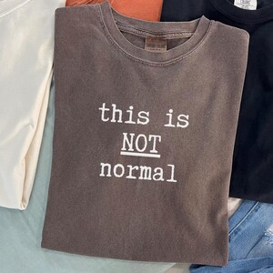 May include: A brown t-shirt with the text "this is NOT normal" printed in white.