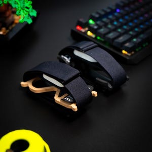 May include: Two pairs of black and beige glasses with a dark blue strap, resting on a black surface. The glasses have a light beige frame and a dark blue strap. A colorful keyboard is in the background.