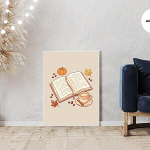 May include: A rectangular wall art print featuring a central illustration of an open book with a pink bookmark, a small orange pumpkin, a steaming cup of coffee on a saucer with a cinnamon stick, scattered coffee beans, and autumn leaves.