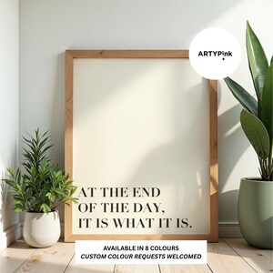 May include: A rectangular wall art print in a light wood frame featuring the black text AT THE END OF THE DAY, IT IS WHAT IT IS. The print includes a circular logo in the top right corner with the text ARTYPink and a black drop icon.