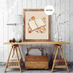 May include: A framed wall art print featuring an illustration of an open book, a coffee cup with a cinnamon stick, a small orange pumpkin, coffee beans, and autumn leaves on a light beige background, with the text ARTYPink in the corner.
