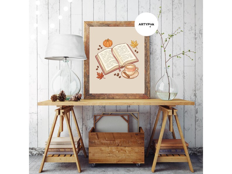 May include: A framed wall art print featuring an illustration of an open book, a coffee cup with a cinnamon stick, a small orange pumpkin, coffee beans, and autumn leaves on a light beige background, with the text ARTYPink in the corner.