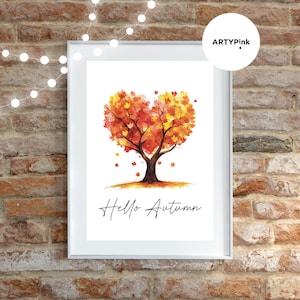 May include: A framed wall art print featuring a watercolor illustration of a tree with a heart-shaped canopy in shades of orange, yellow, and red. The text "Hello Autumn" is printed in black script below the tree on a white background.