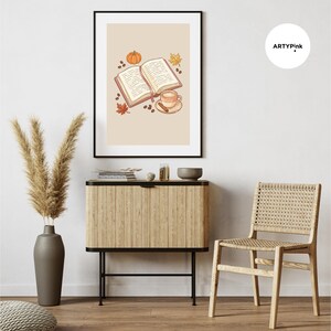 May include: A framed wall art print featuring an open book, a coffee cup with a cinnamon stick, a small pumpkin, and autumn leaves on a light beige background. The text ARTYPink is visible in a white circle in the upper right corner of the image.