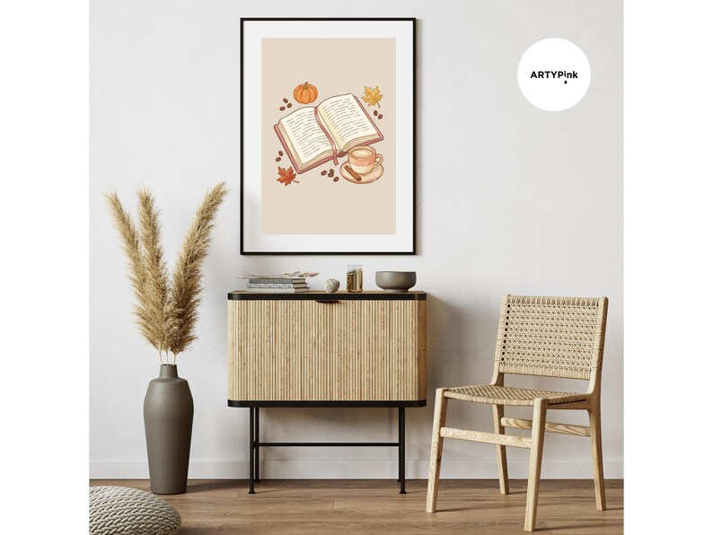 May include: A framed wall art print featuring an open book, a coffee cup with a cinnamon stick, a small pumpkin, and autumn leaves on a light beige background. The text ARTYPink is visible in a white circle in the upper right corner of the image.