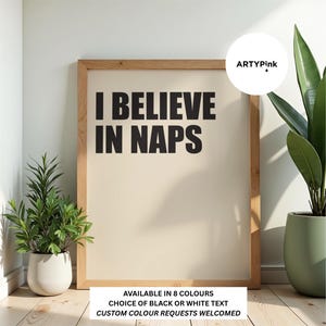 May include: A rectangular wall art print in a light wooden frame featuring the black text I BELIEVE IN NAPS on a cream background. The print includes a circular logo with the text ARTYPink and a bottom label stating AVAILABLE IN 8 COLOURS, CHOICE OF BLACK OR WHITE TEXT, CUSTOM COLOUR REQUESTS WELCOMED.