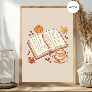 May include: A framed wall art print featuring an open book with a pink bookmark, a pumpkin, a coffee cup on a saucer with a cinnamon stick, scattered coffee beans, and two autumn leaves on a light beige background with the text ARTYPINK.