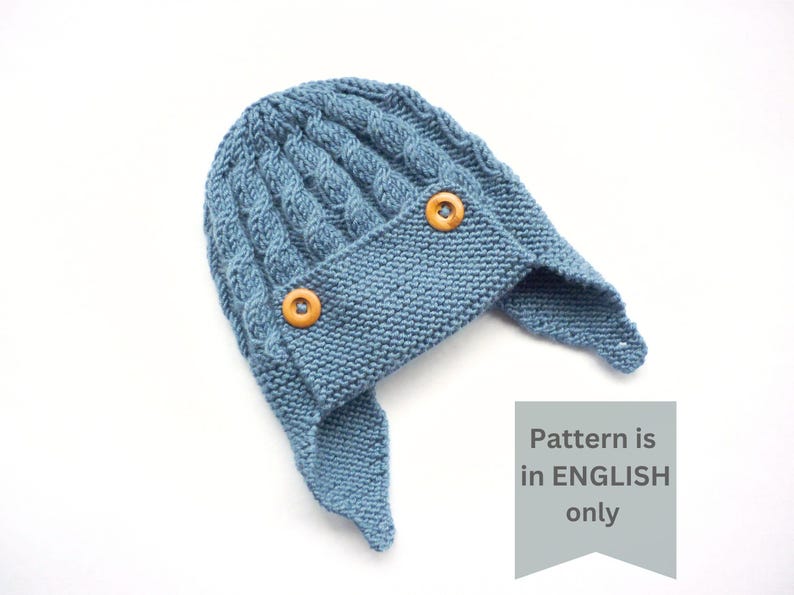 May include: A blue knitted hat with ear flaps and two wooden buttons. The pattern is in English only.