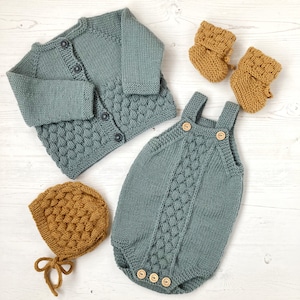 Puede incluir: Un conjunto de ropa de punto para bebé en verde salvia y amarillo mostaza. El conjunto incluye un cárdigan, un pelele, un gorro y botines.