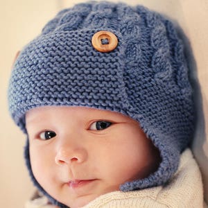 A knitting pattern for a baby or child’s aviator hat. The aviator flap is knit in garter stitch and held in place with two buttons. The hat has a simple cable design. Ear flaps cover the ears and can be fastened under the chin with a single button.