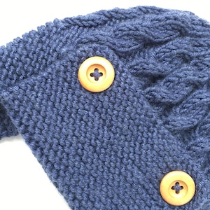 May include: A blue knitted hat with a cable knit pattern and two wooden buttons.