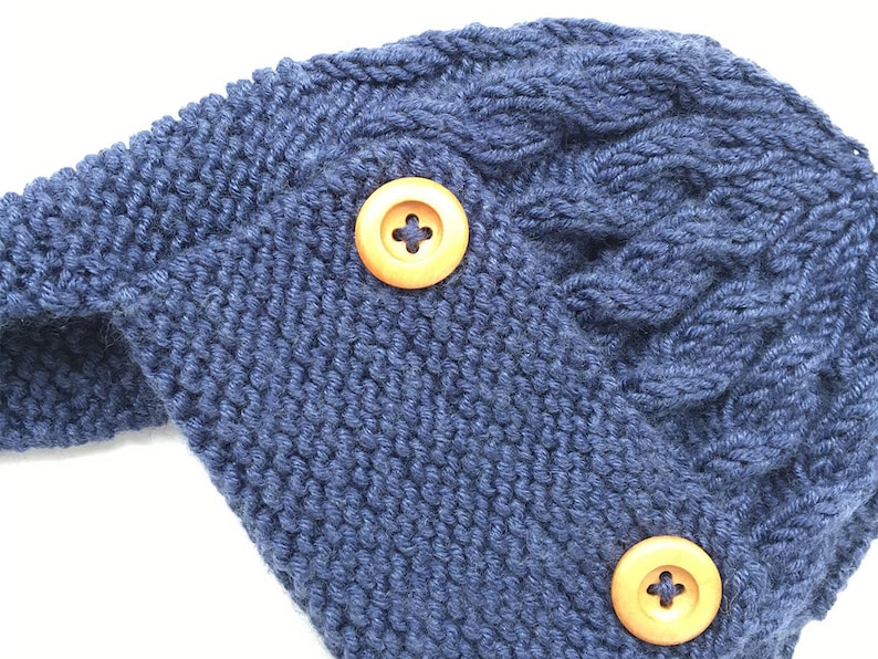 May include: A blue knitted hat with a cable knit pattern and two wooden buttons.