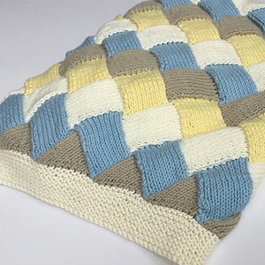 K&ouml;nnte beinhalten: Eine gestrickte Babydecke mit einem karierten Muster in Blaut&ouml;nen, Gelb, Wei&szlig; und Braun.
