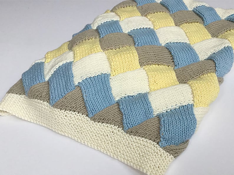 K&ouml;nnte beinhalten: Eine gestrickte Babydecke mit einem karierten Muster in Blaut&ouml;nen, Gelb, Wei&szlig; und Braun.