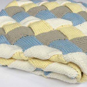 May include: A knitted baby blanket with a woven pattern in shades of white, yellow, light blue, and gray.