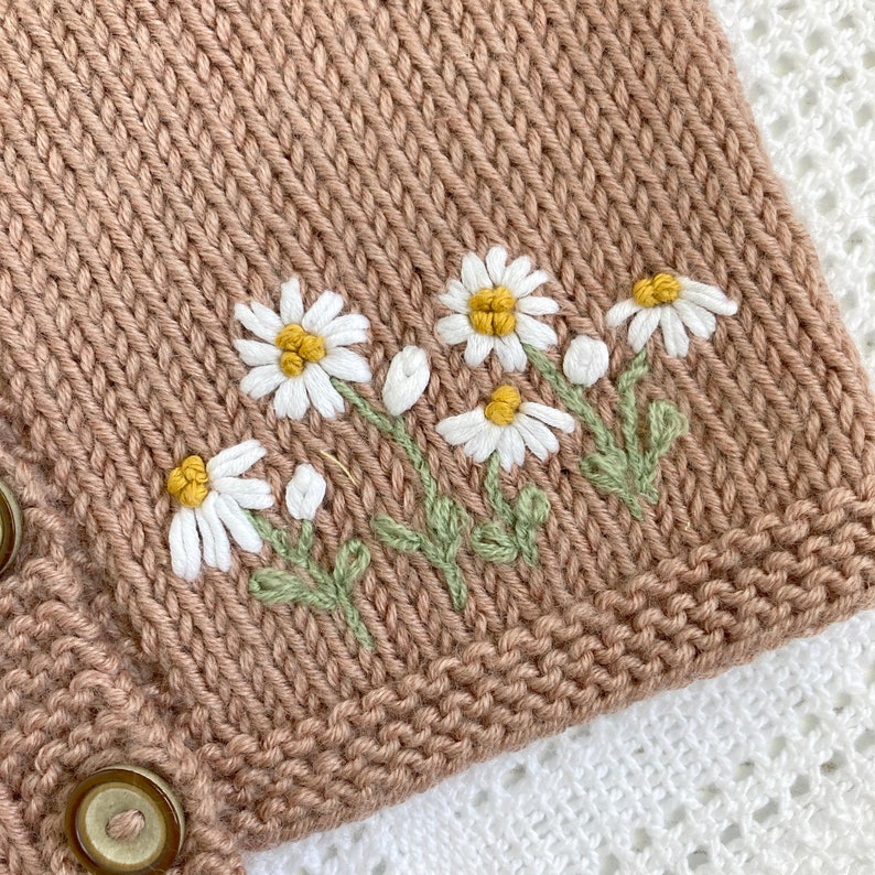 May include: A brown knitted cardigan with embroidered white daisies and green stems.