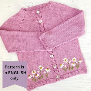 May include: A pink knitted cardigan with a button closure and embroidered daisies on the front. The pattern is in English only.