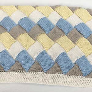 K&ouml;nnte beinhalten: Eine gestrickte Babydecke mit einem gewebten Muster in den Farben Gelb, Wei&szlig;, Blau und Grau.