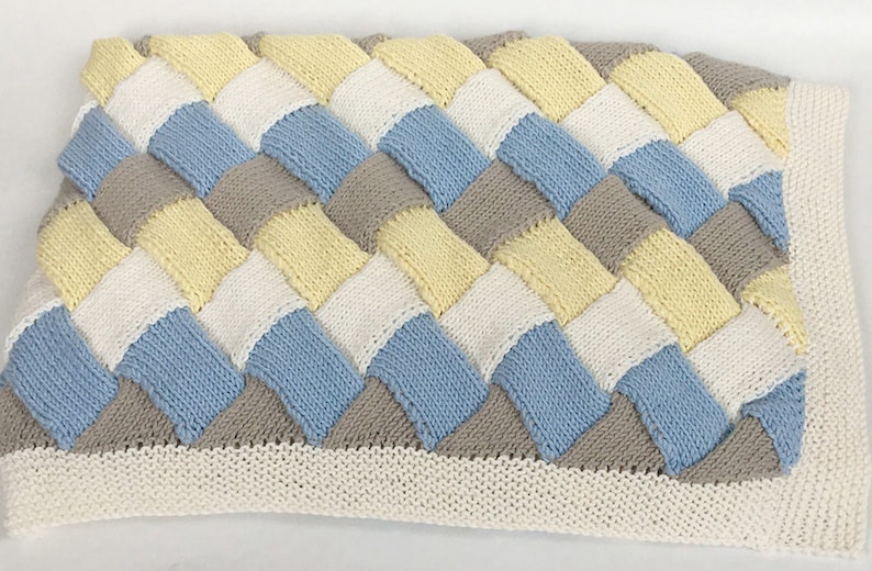 K&ouml;nnte beinhalten: Eine gestrickte Babydecke mit einem gewebten Muster in den Farben Gelb, Wei&szlig;, Blau und Grau.