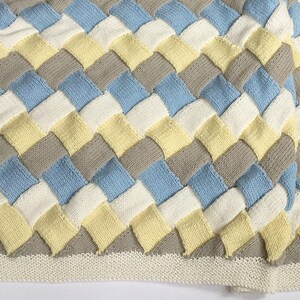 K&ouml;nnte beinhalten: Eine gewebte Babydecke in Blaut&ouml;nen, Gelb und Grau. Die Decke ist mit einem einfachen Strickmuster gearbeitet und hat eine strukturierte, gewebte Optik.