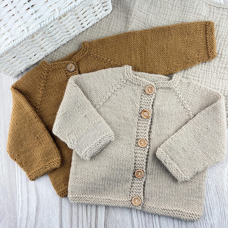 May include: Two long-sleeve knit cardigans, one in a solid mustard yellow and one in a solid light beige. Each cardigan features a round neckline, ribbed cuffs, and a vertical row of five small, round, light brown wooden buttons down the front.