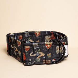Puede incluir: Un collar negro para mascotas con un patrón repetitivo de iconos mágicos coloridos que incluyen escudos, sombreros puntiagudos y plantas en macetas. El collar incluye herrajes de metal negro, una anilla en D y una etiqueta de marca de tela blanca.