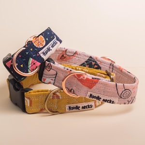 Può includere: Tre collari per animali domestici con motivi in tessuto blu navy, rosa chiaro e giallo senape. Ogni collare include una fibbia in plastica nera, un anello a D in metallo oro rosa e un'etichetta in tessuto bianco con la scritta Noodle necks.