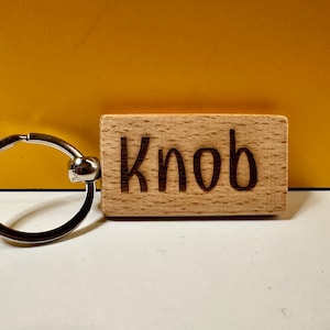 May include: A wooden keyring with a silver ring and the word "Knob" engraved on it.