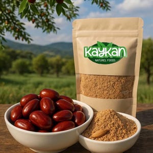 May include: A product shot featuring a kraft paper bag with the "kaykan naturel foods" logo, alongside two white bowls filled with reddish-brown dates and date powder. A single almond sits atop the powder. Green foliage and a blurred landscape form the background.