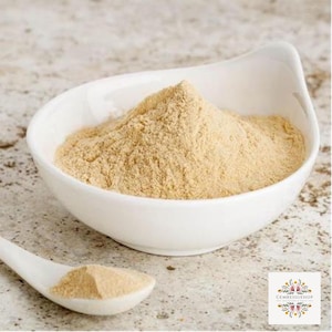 May include: A white bowl filled with a light brown powder. The powder is a natural ingredient used in cooking and baking.