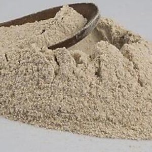 May include: A pile of light brown flour with a wooden spoon partially submerged in it.