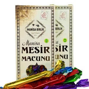 Könnte beinhalten: Zwei Schachteln mit "Manisa Mesir Macunu"-Bonbons mit farbenfrohen, einzeln verpackten Stücken im Vordergrund. Die Schachteln haben verzierte Ränder und Text auf Türkisch. Die Süßigkeiten sind gold, rot, lila, grün und blau.