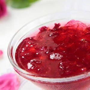 Könnte beinhalten: Eine klare Glasschüssel gefüllt mit roter Rosenblütenmarmelade. Die Marmelade ist dickflüssig und hat einen glänzenden Überzug.