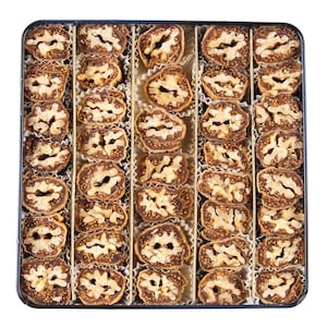 May include: A square tin containing rows of chocolate-covered walnut halves, each in a paper cup. The arrangement presents a neat display of a sweet confection, perfect for gifting or enjoying.